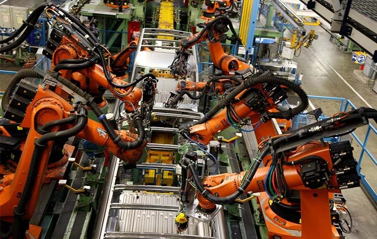 ramiona robotów pracujące na taśmie produkcyjnej